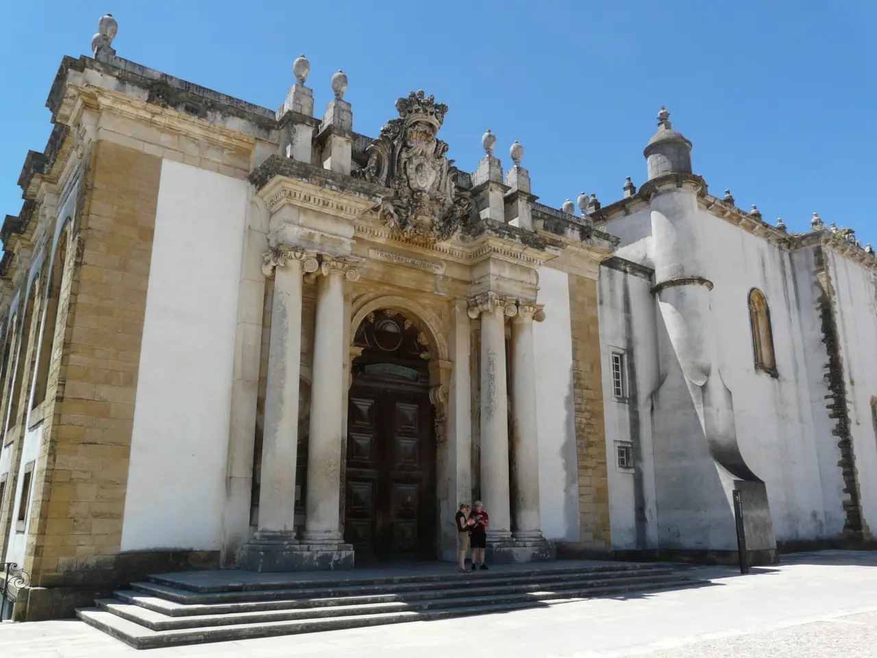 The baroque stone portal of the Biblioteca Joanina library at the University of Coimbra, Portugal, with columns and a royal coat of arms above the door