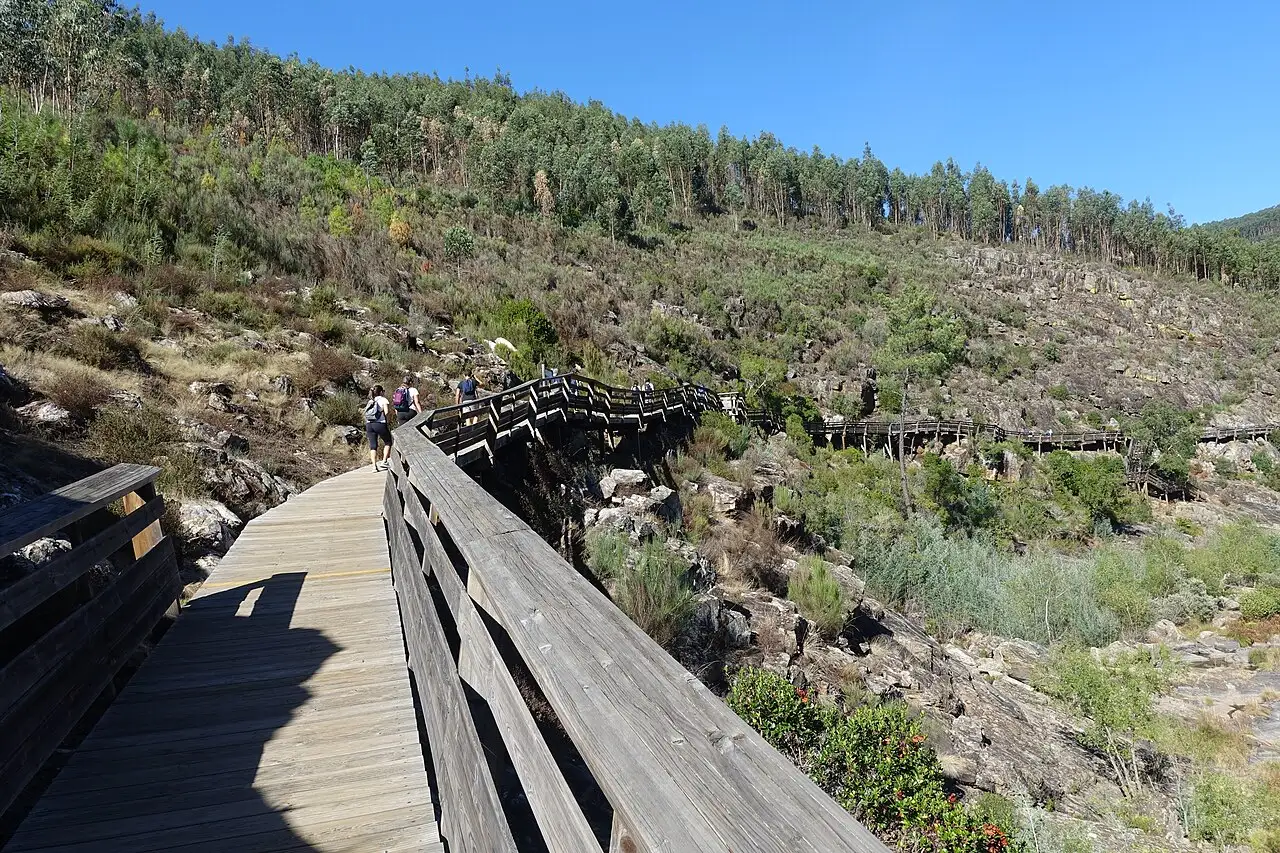 Hikers on the Passadiços do Paiva wooden walkway climbing along a rocky hillside above the Paiva river in the Arouca Geopark, Portugal